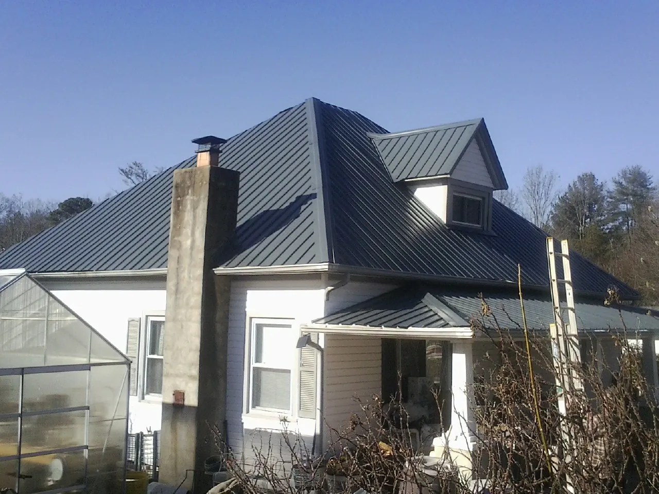 Dark blue standing seam metal roof on a white farmhouse with dormer — Slate & Tile Roof Repair by Roofing Brothers in West Edmeston