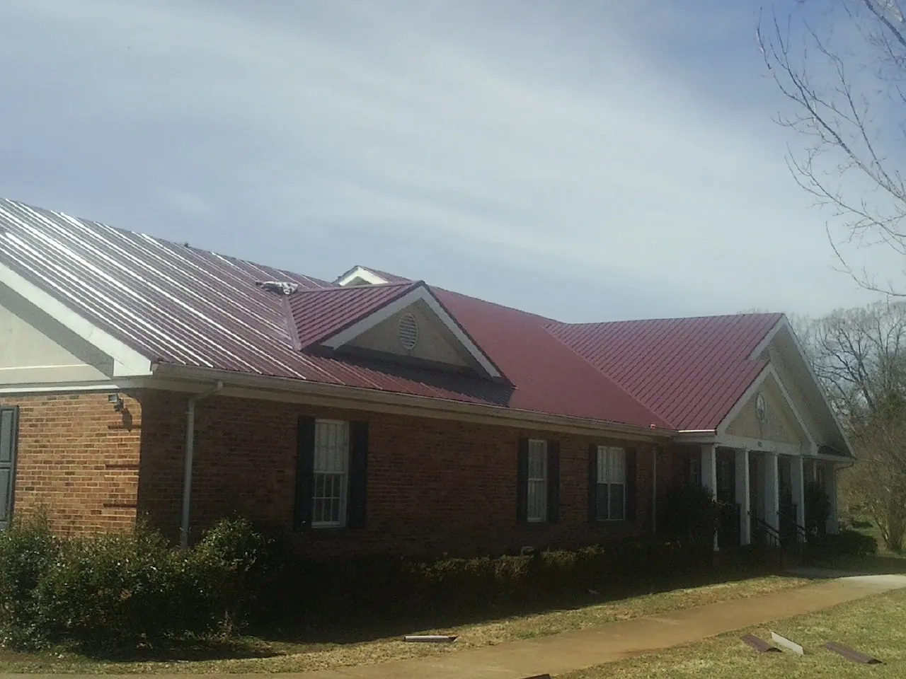 Red metal roof with gabled entries on a long brick building, from a Hail Damage Roof Repair job in West Edmeston