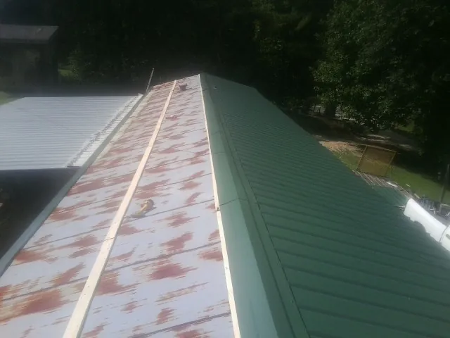 Old rusted panels beside newly installed green metal roofing — Wind Damage Roof Repair by Roofing Brothers in West Edmeston