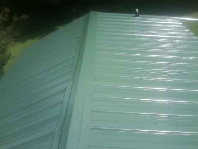 New green metal panels meeting at the ridge of a roof — Flat Roof Repair work by our crew in West Edmeston