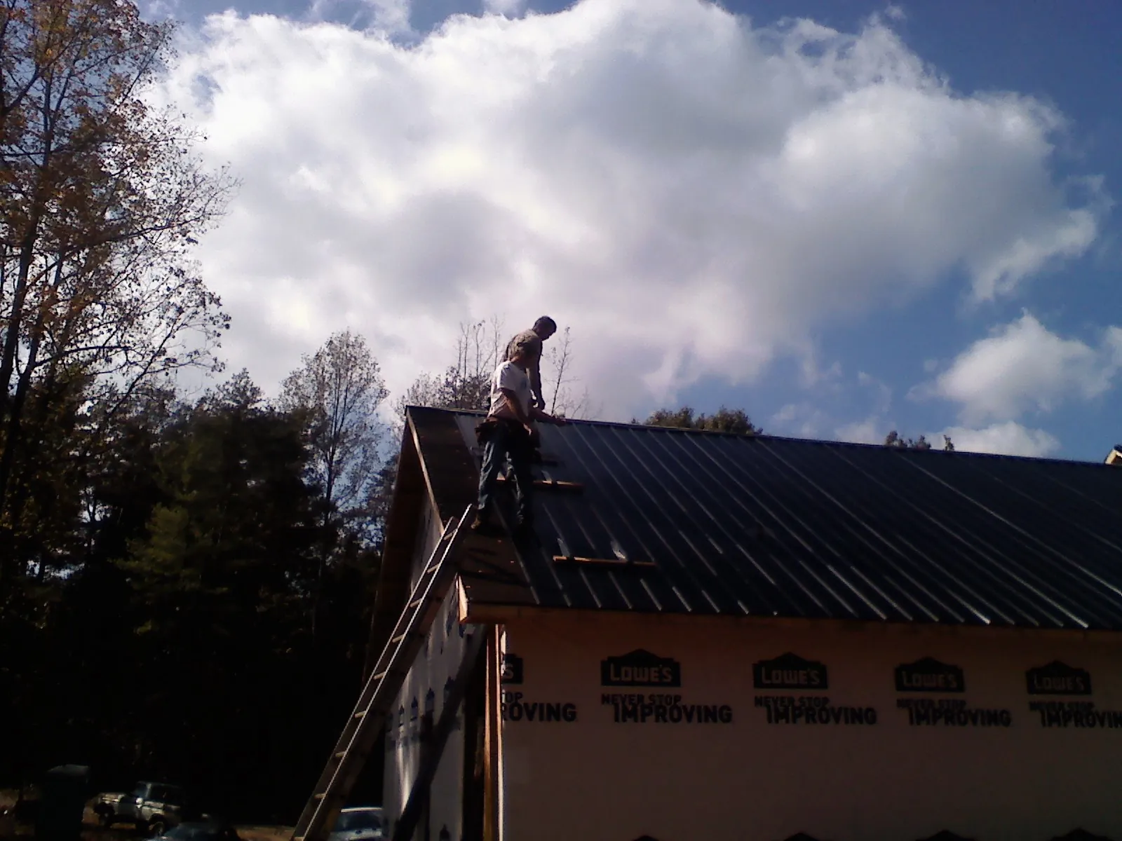 Roofer fastening dark metal panels high against a cloudy sky, from a Roof Inspection job in West Edmeston