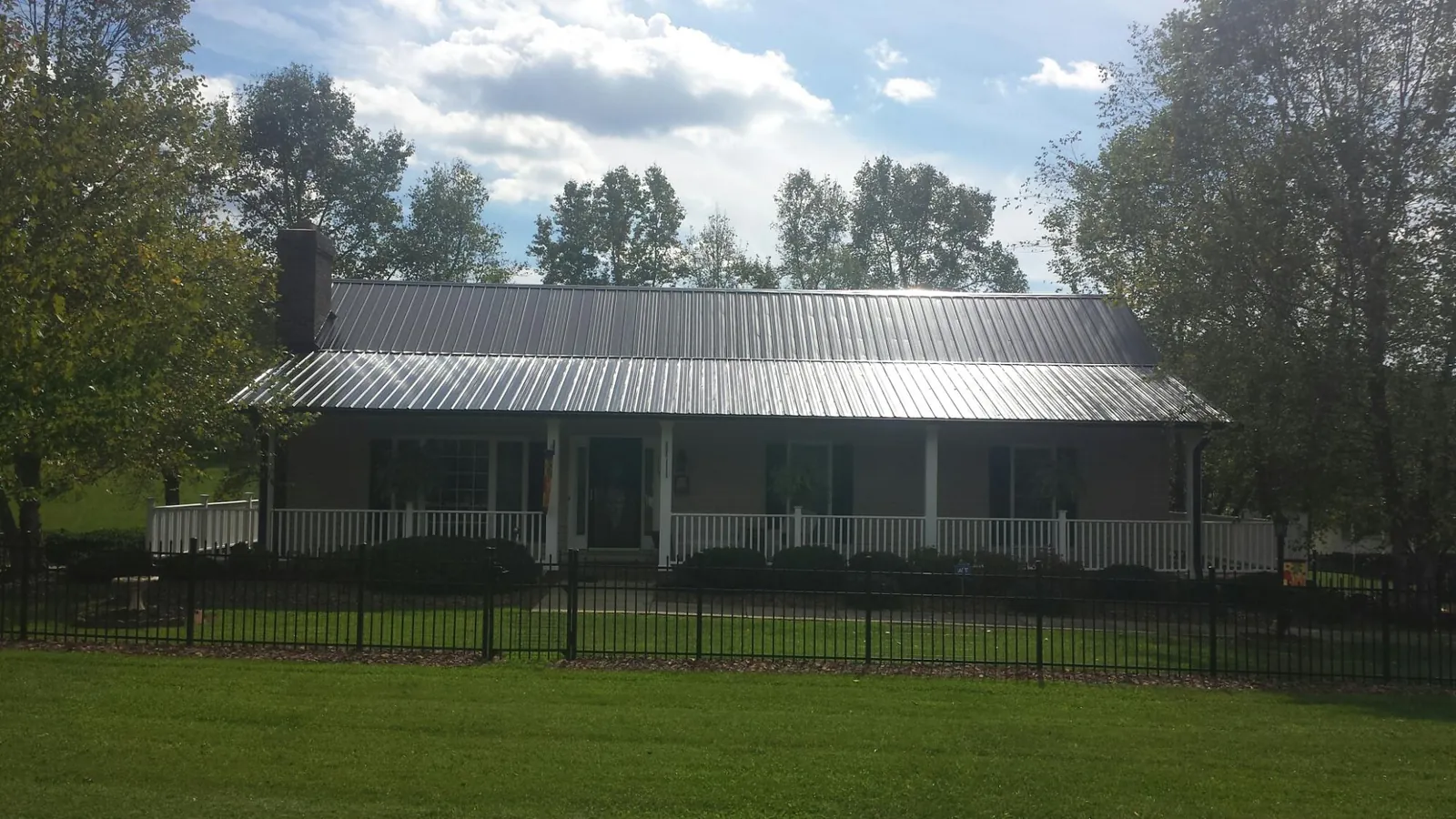 Gray metal roof on a brick ranch with a full width front porch — Gutter Guard Installation work by our crew in West Edmeston