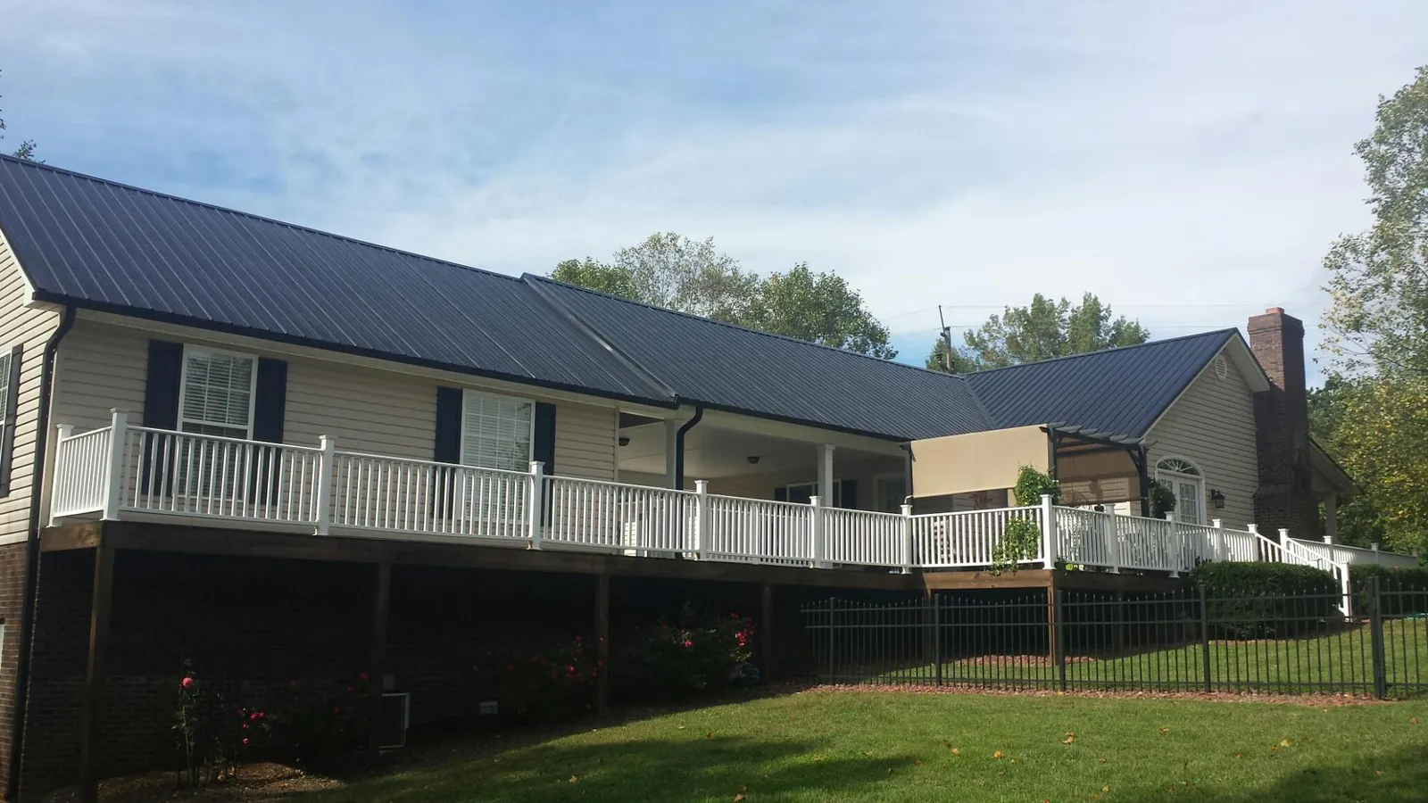 Black metal roof above a long white railed deck on a hillside home in West Edmeston