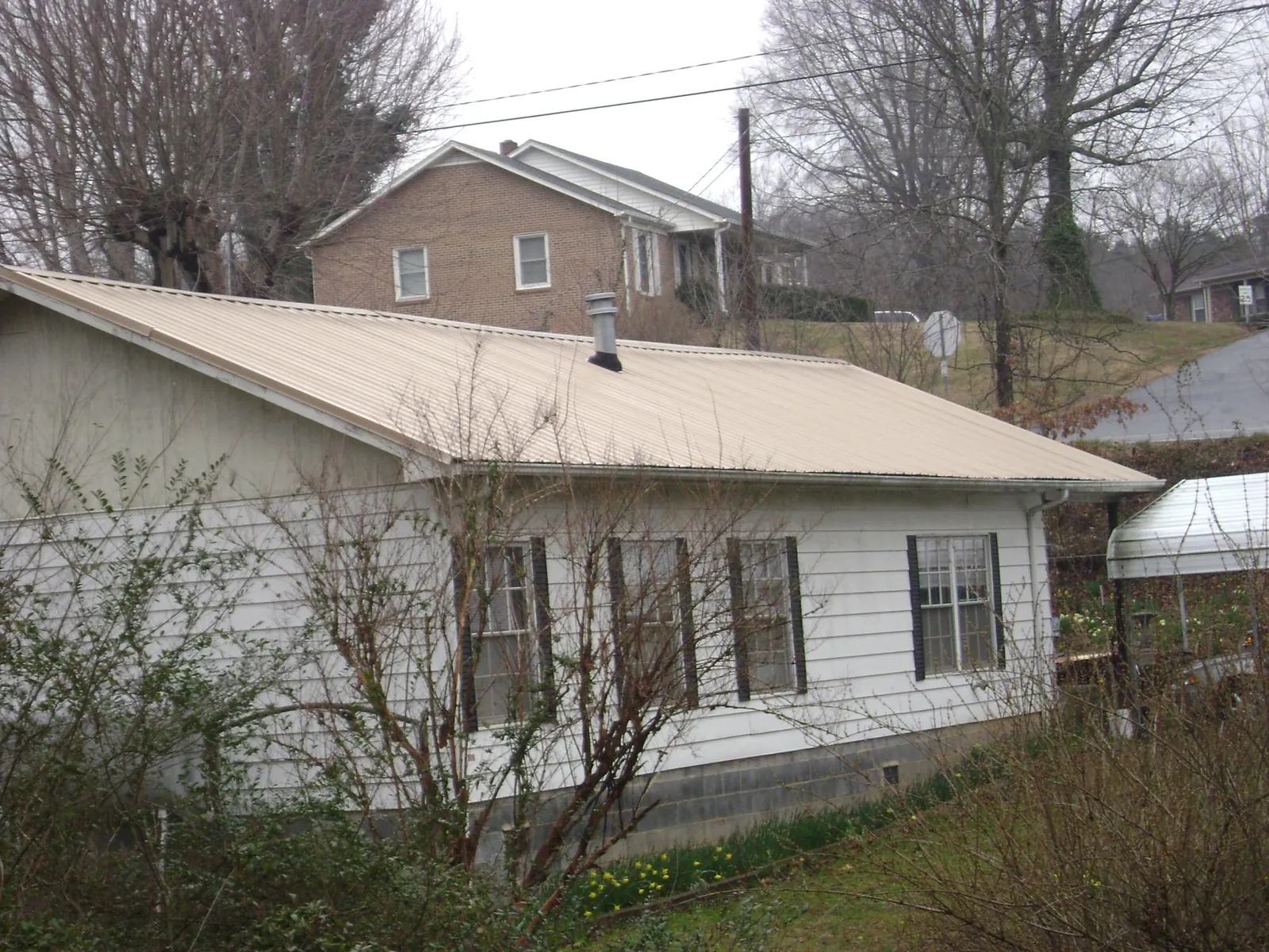 Tan metal roof on a white sided house set into a hillside — Commercial Roofing by Roofing Brothers in West Edmeston