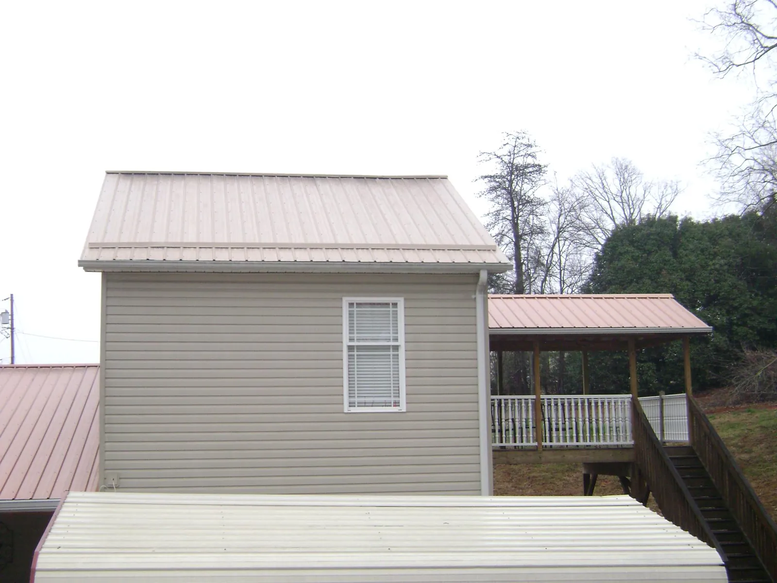 Tan metal roofs on a two story addition and attached porch, from a Roof Replacement job in West Edmeston